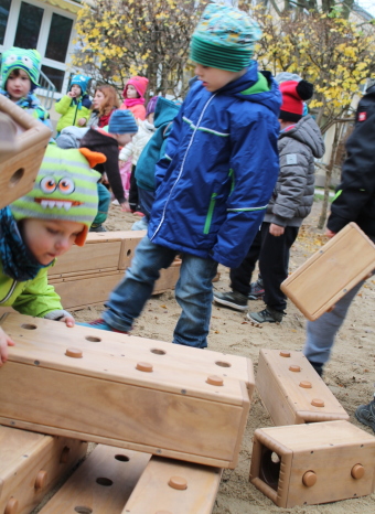 Auf dem Bild sind Kinder, die mit großen Bausteinen im Sandkasten spielen, zu sehen