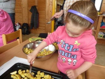 Auf dem Bild ist ein Mädchen zusehen, dass die Kartoffeln auf dem Blech mit Olivenöl bestreicht