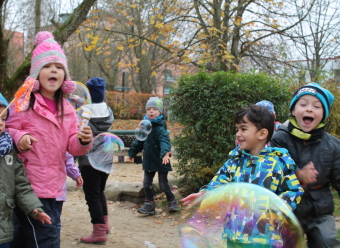 Auf dem Bild sind mehrere Kinder und Seifenblasen im Garten zu sehen