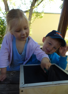 Kinder spielen mit einem Fühlkasten an einem Tisch im Garten