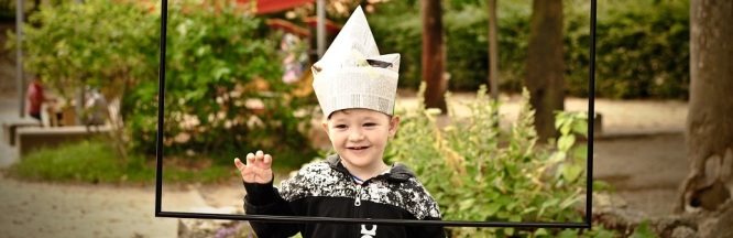 Auf dem Bild ist ein Kleinkind mit dem Hut aus Papier im Garten zu sehen