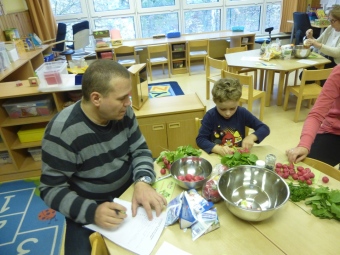 Auf dem Bild ist ein Vater mit seinem Sohn an einem Tisch mit einem Rezept und verschiedenen Gemüse zu sehen