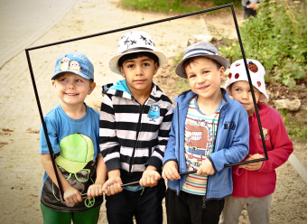 Auf dem Bild sind 4 Kinder mit aufgesetzten Hüten beim Fotografieren zu sehen