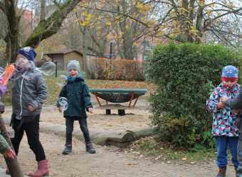 Auf dem Bild sind Kinder, die Seifenblasen pusten und lachen, im Garten zu sehen