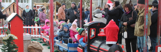 Auf dem Bild sind Erwachsene und Kinder am Weihnachtsmarkt im Garten zu sehen