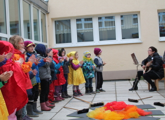 Auf dem Bild sind Kinder und eine Erzieherin singend zu sehen