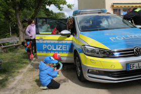 Kinder, eine Frau und ein Polizist stehen an einem Polizeiauto.