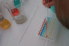 Hand eines Kindes tropft mit Pipette auf eine Auftragematte wie im Labor