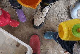 Mehrere Gummistiefel von oben im Sand bei nassem Wetter